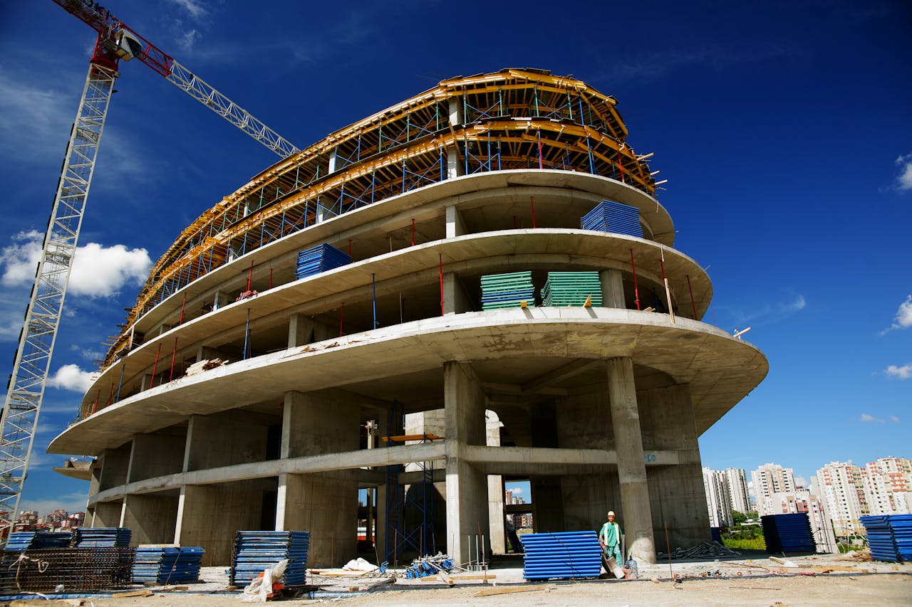 about-us Low angle view of a circular building under construction with a crane, clear blue sky.