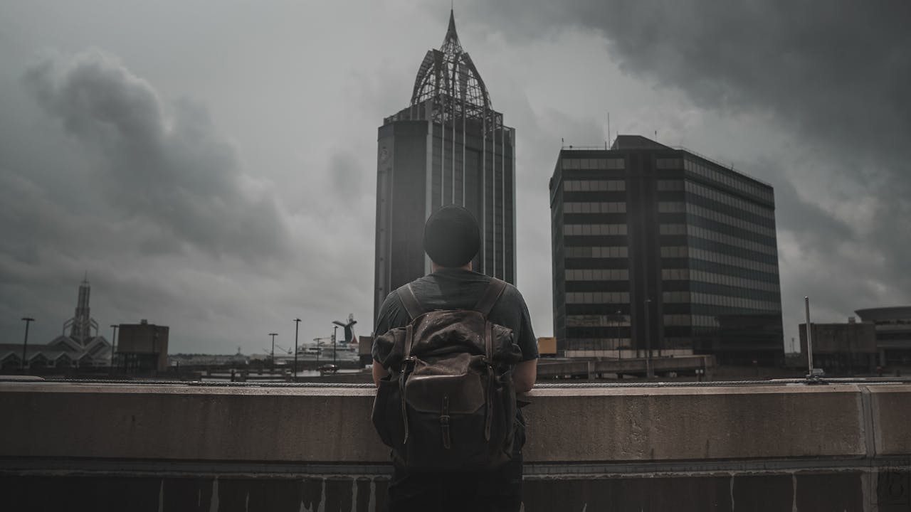 A man with a backpack overlooks the Mobile AL skyline under dramatic clouds.