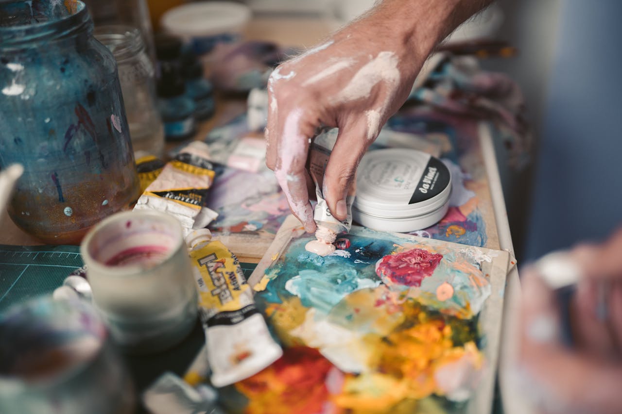 why-choose-us A detailed view of an artist's hand mixing vivid oil paints with a palette knife.